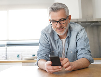 Gen X male leaning on kitchen counter typing on his cellphone